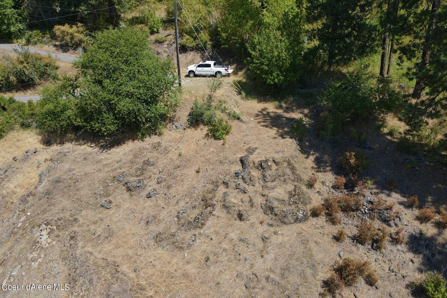 Aerial view of a dry, rocky vacant lot bordered by trees and brush, with a road along its edge.