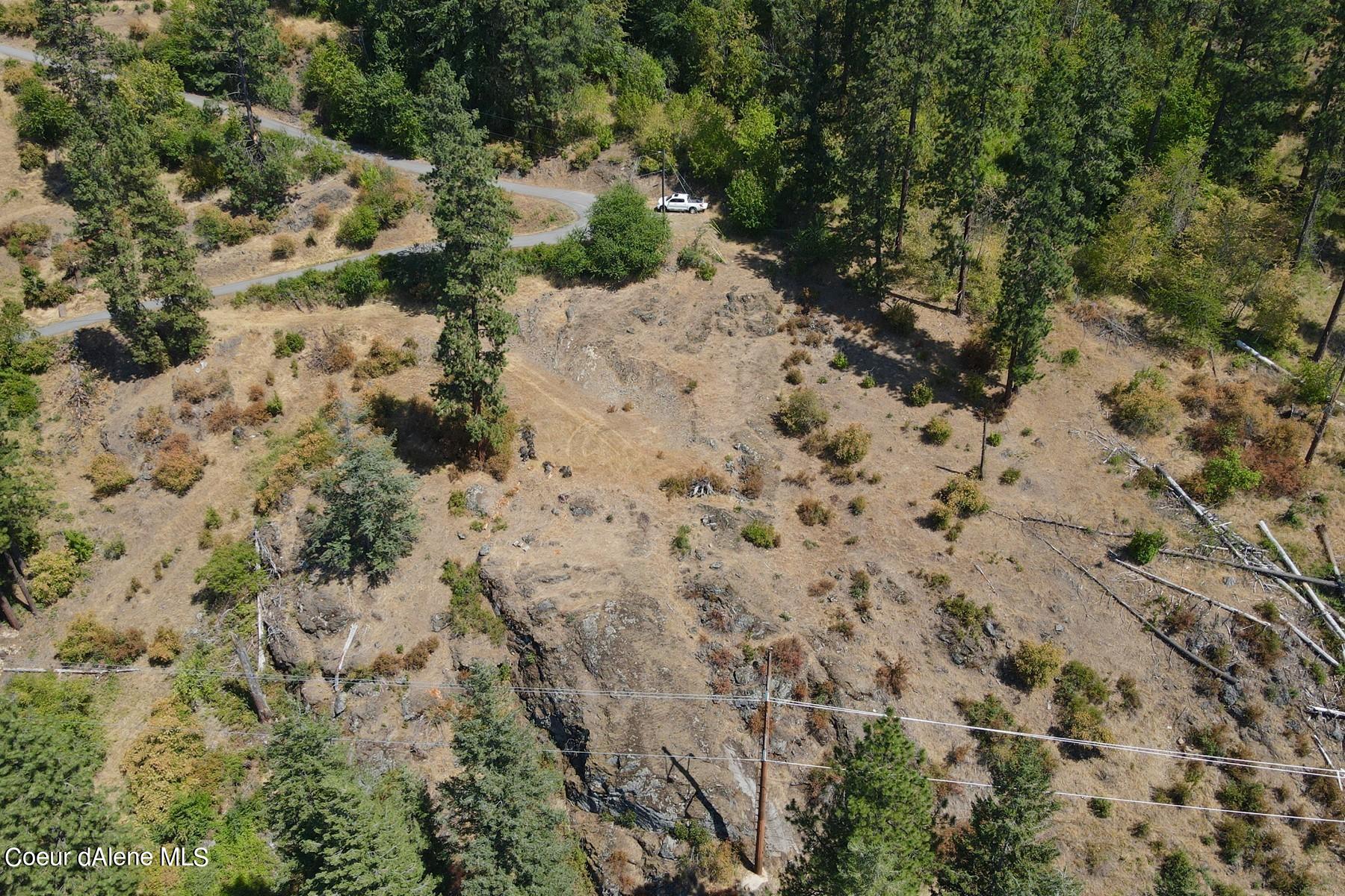 Aerial view of a rocky, partially cleared parcel bordered by trees, with a curving road and utility lines.