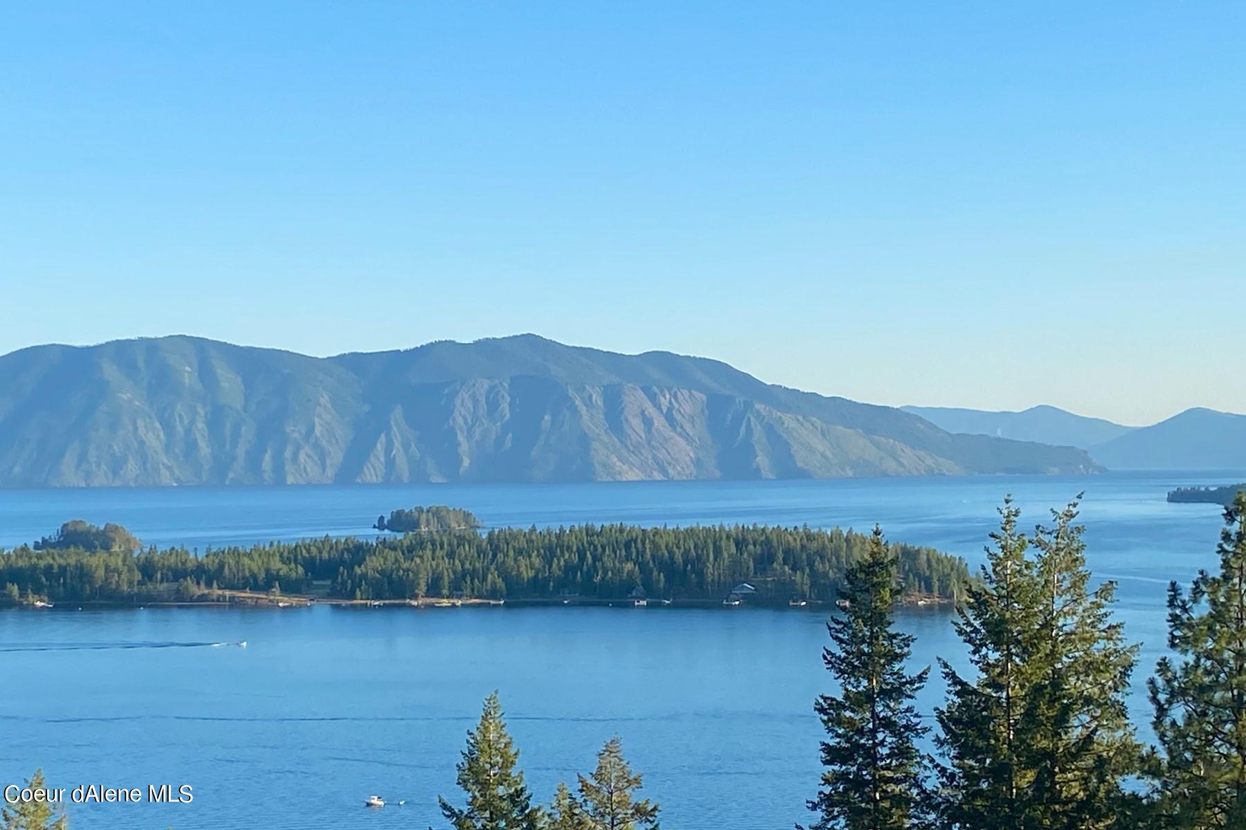 Blue lake, evergreen shoreline, and rugged mountains viewed from above.