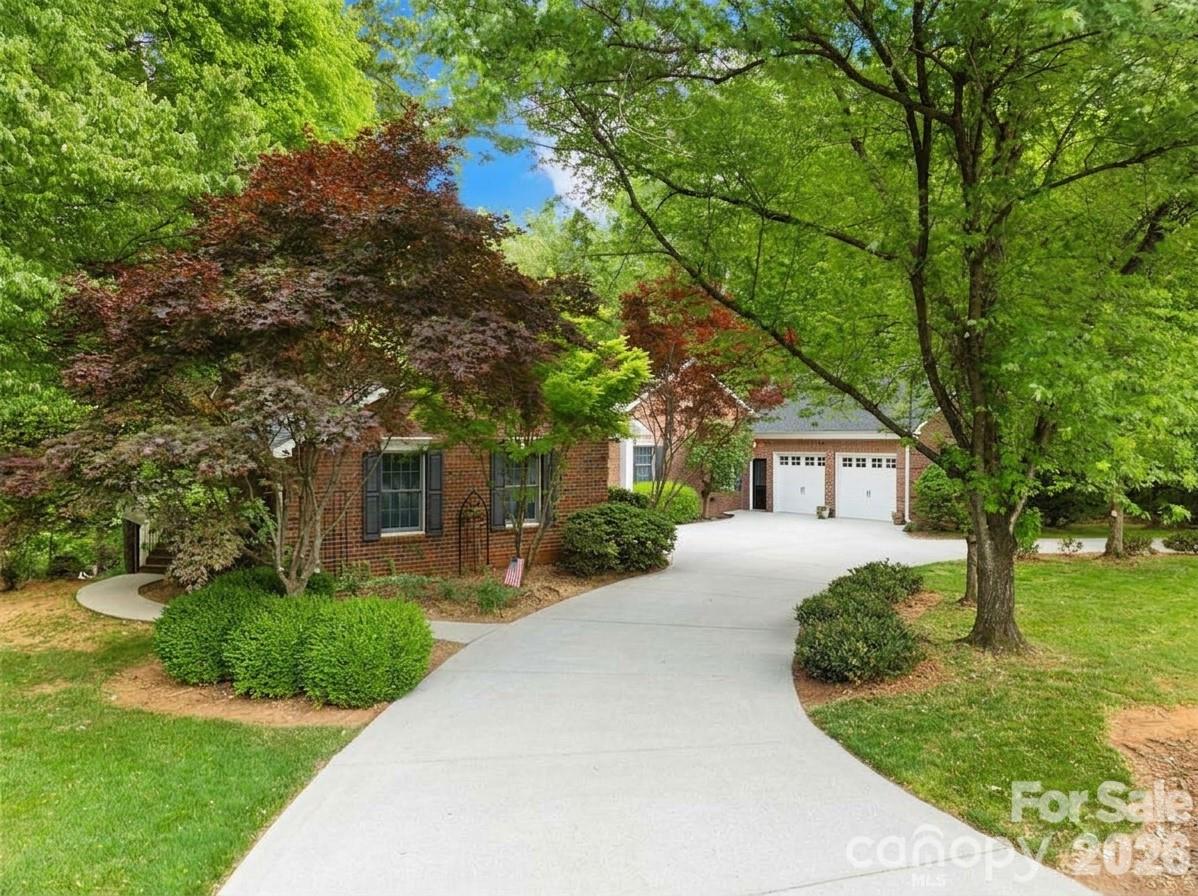 Brick house with a two-car garage and a broad driveway beneath mature trees.