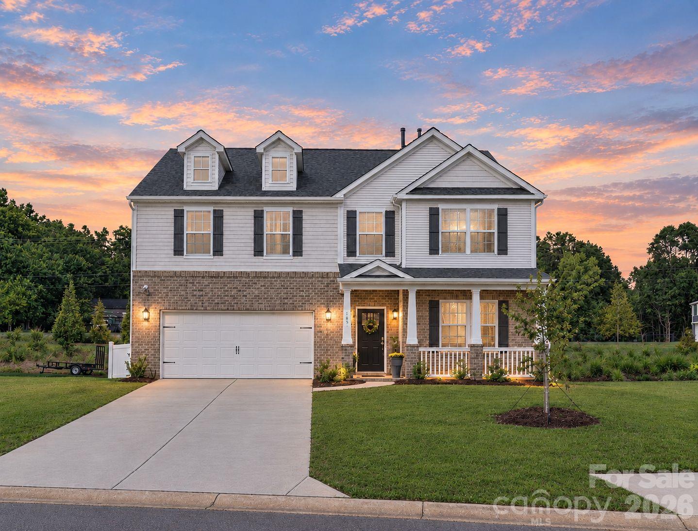Two-story white-and-brick home with an attached garage and covered porch at dusk.