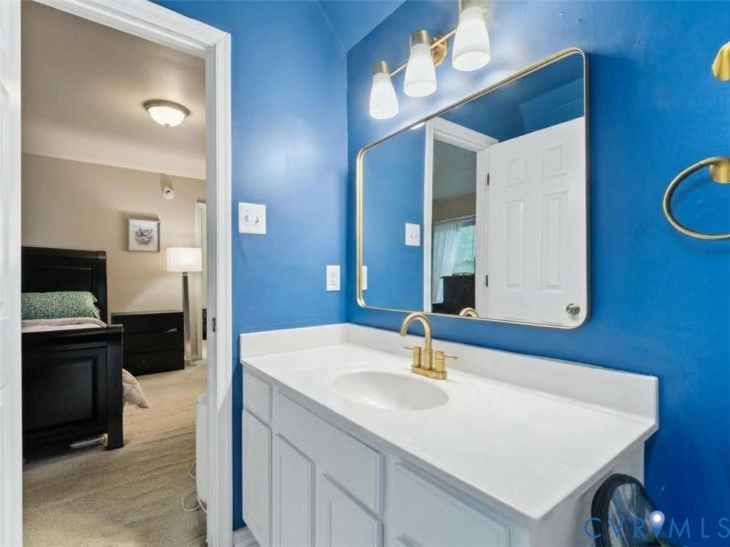 Bathroom with a white vanity against bright blue walls, opening to a furnished bedroom.