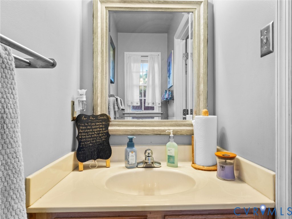 Bathroom vanity with cream countertop, oval sink, framed mirror, and guest toiletries.