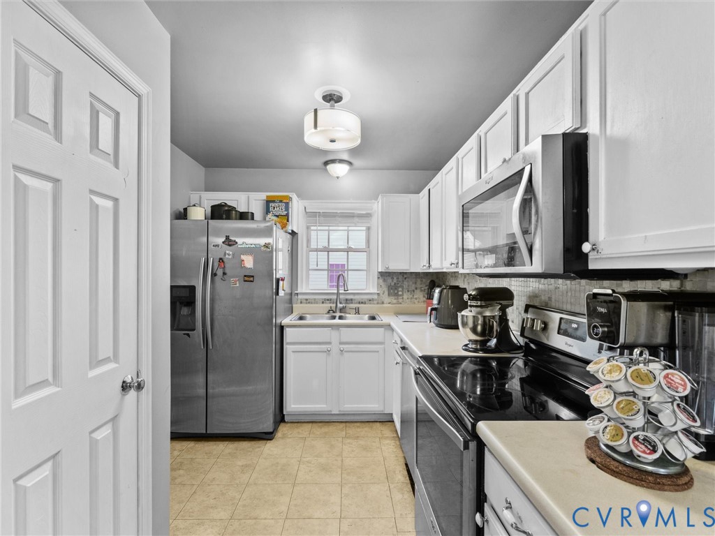 Kitchen with white cabinets, stainless-steel appliances, a rear window, and a coffee-pod carousel.