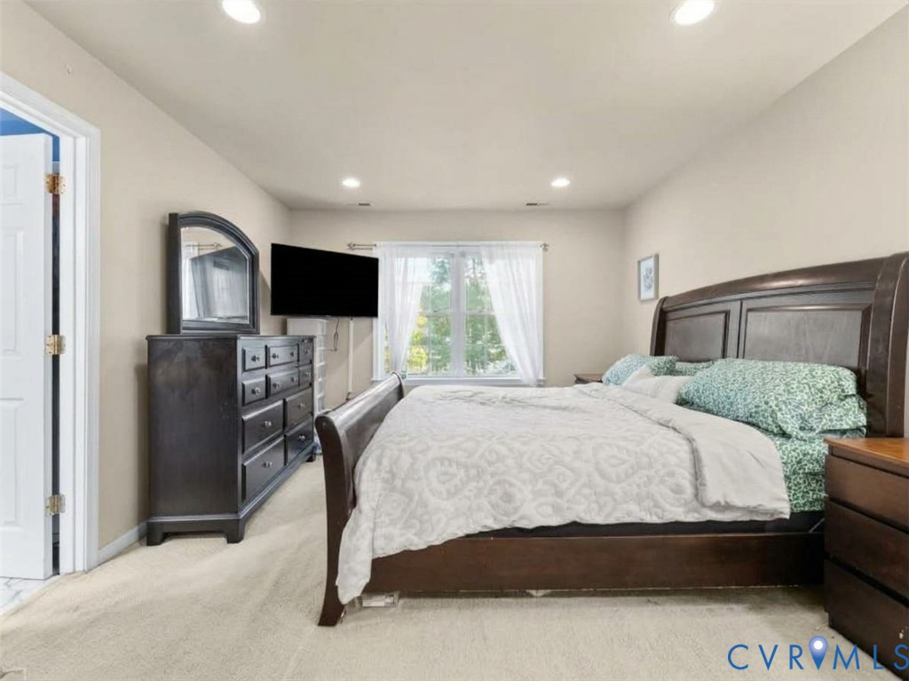 Furnished bedroom with a dark wood bed, green patterned pillows, and a window with sheer curtains.