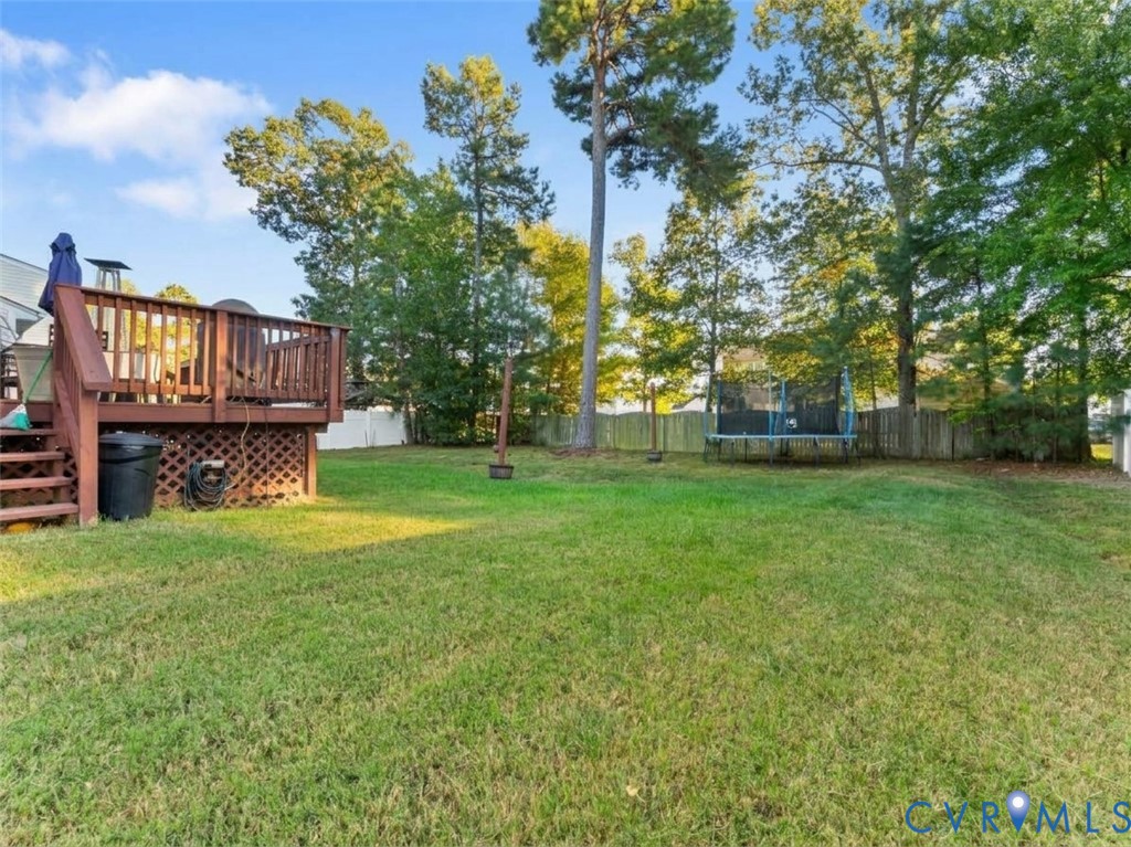 Fenced backyard with a raised wooden deck, trampoline, and mature trees.
