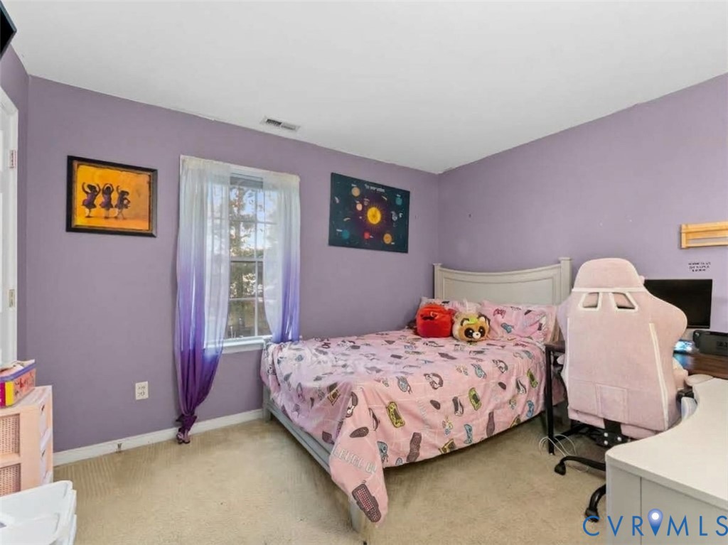 Bedroom with lavender walls, pink patterned bedding, and a pale pink gaming chair by the desk.
