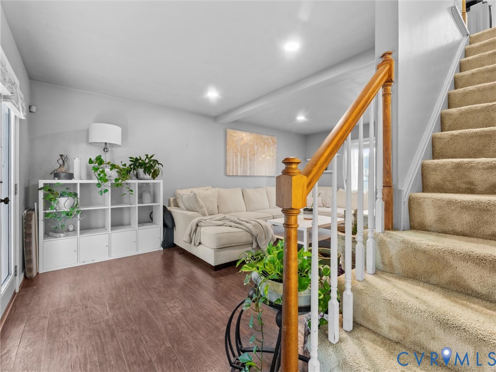 Furnished living room with beige sectional, plant-filled shelving, and carpeted staircase.