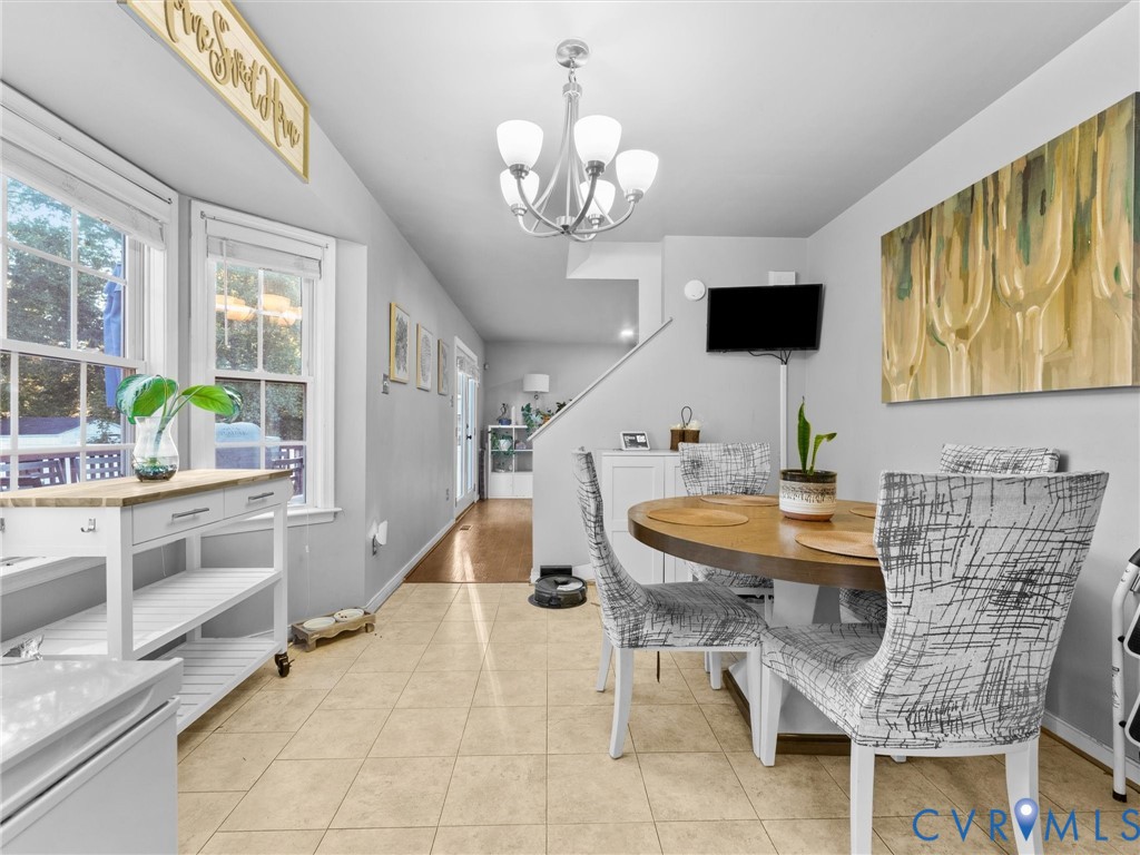 Dining area with a round wood table, patterned chairs, chandelier, and large windows.
