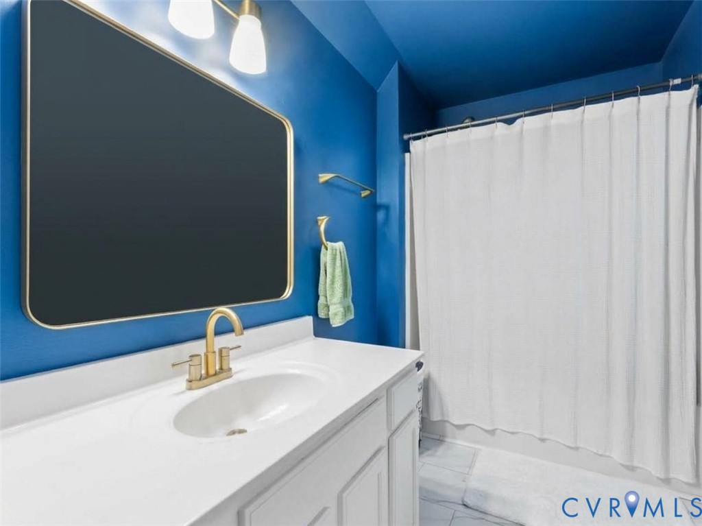 Bathroom with vivid blue walls, a white vanity, gold fixtures, and a white shower curtain.