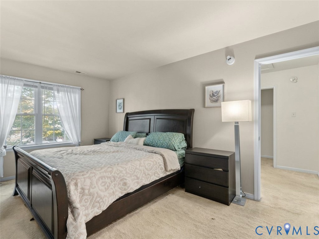 Bedroom with a dark wood bed, teal pillows, sheer-curtained window, and adjoining doorway.