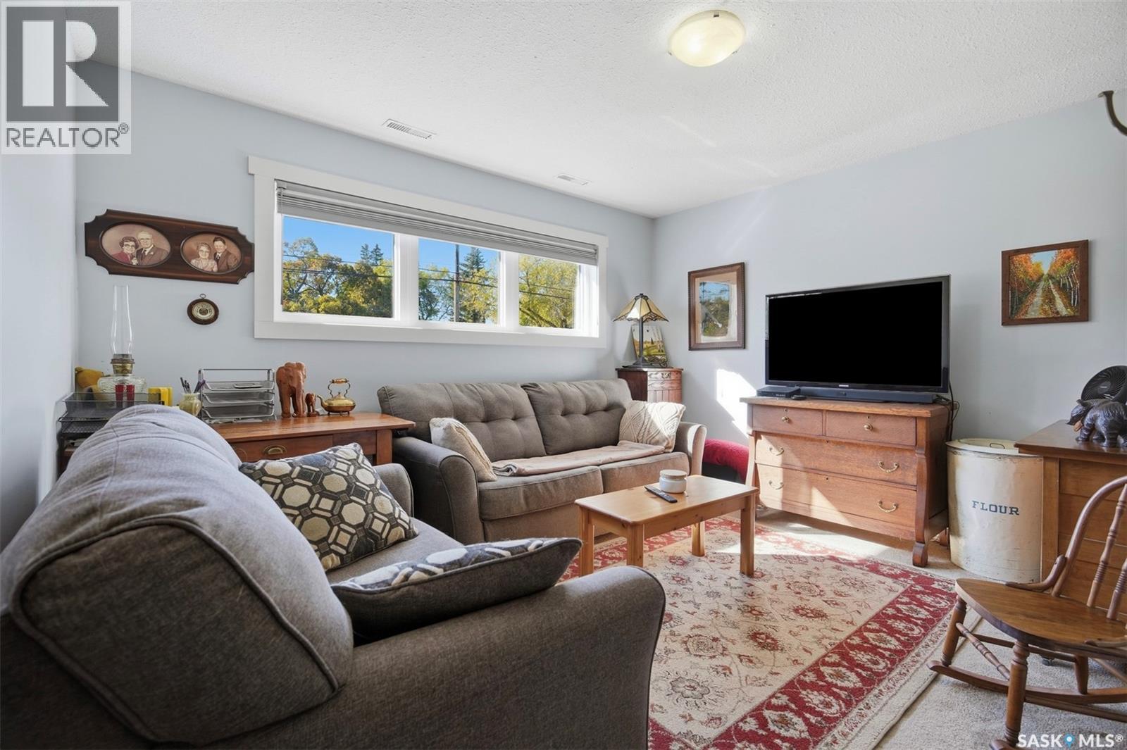 Furnished living room with gray sofas, a patterned rug, and a wide window overlooking trees.