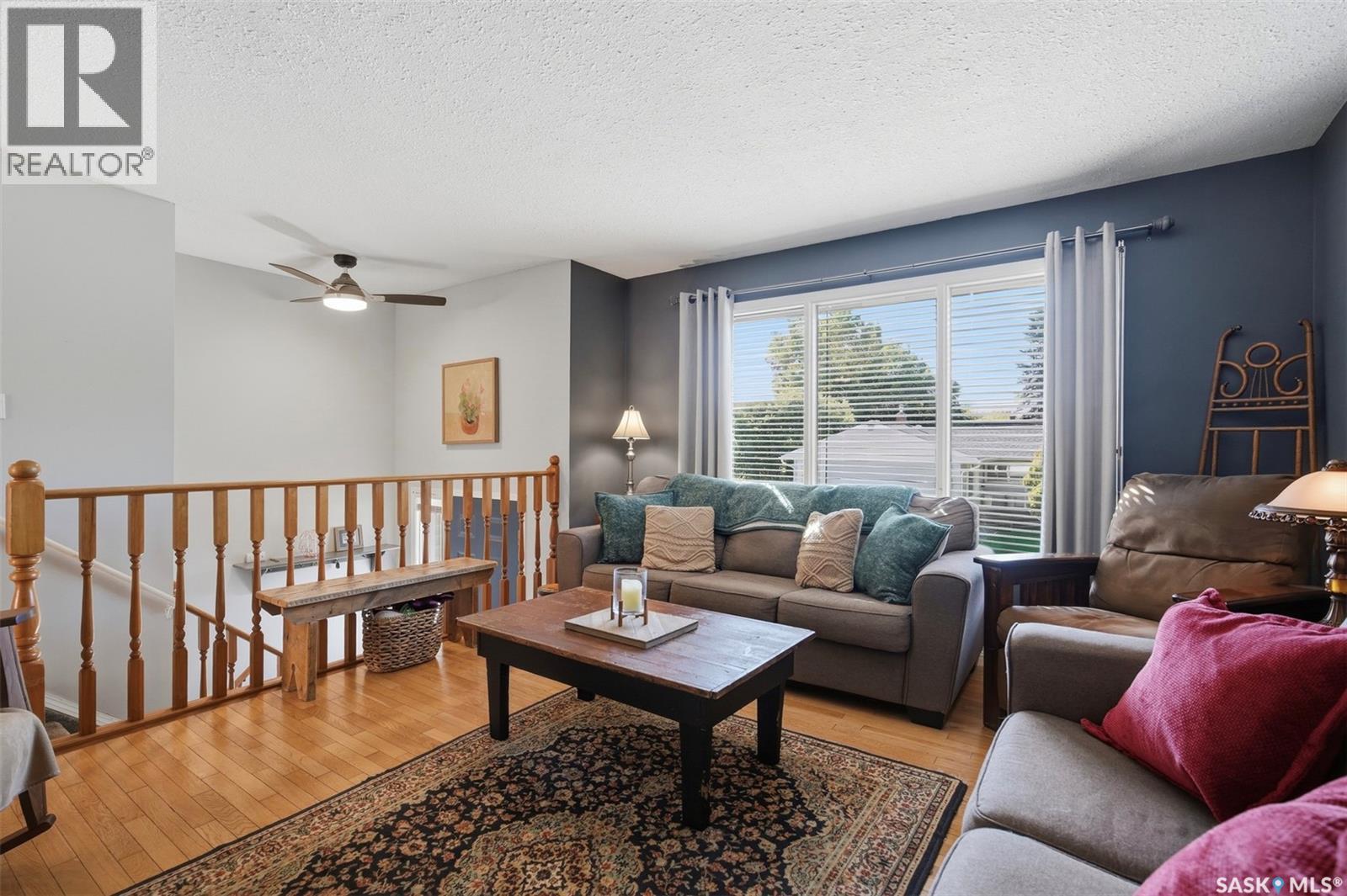 Living room with blue accent wall, large window, hardwood floors, and a wooden stair railing.
