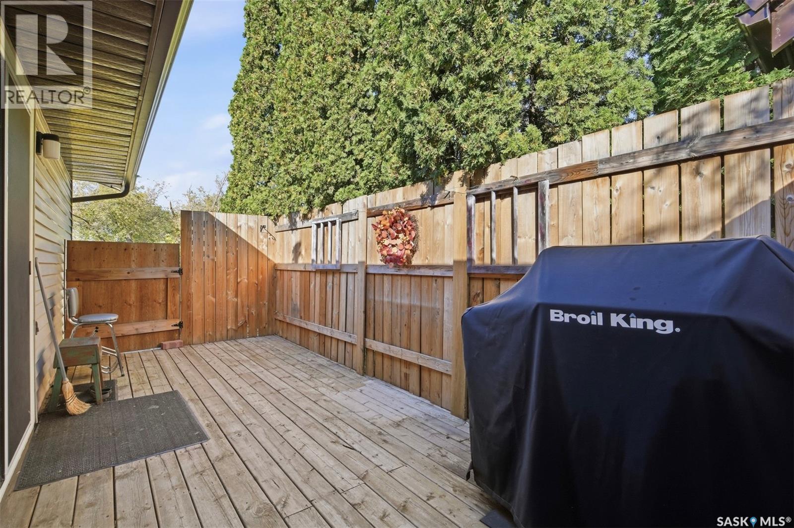 Wooden backyard deck enclosed by a tall fence, with a covered Broil King grill.