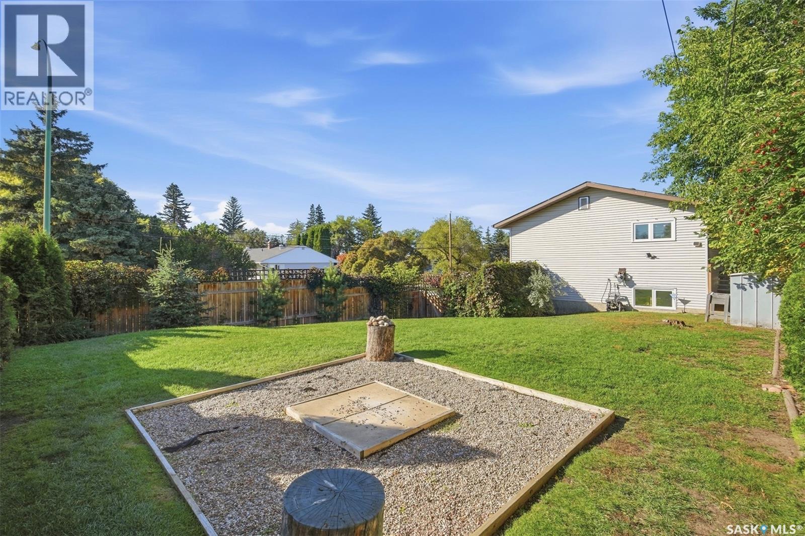 Backyard with a fenced lawn, gravel seating area, and mature trees beside the house.