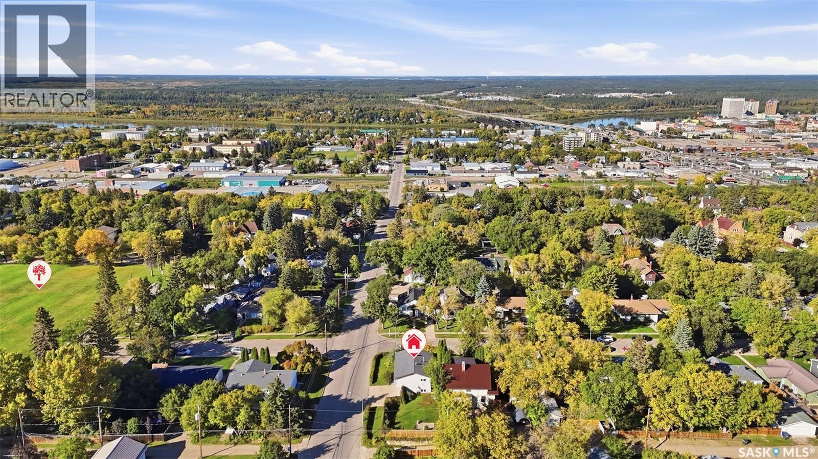 Aerial view of a tree-lined residential neighborhood, with the featured home marked near the foreground and a river beyond.