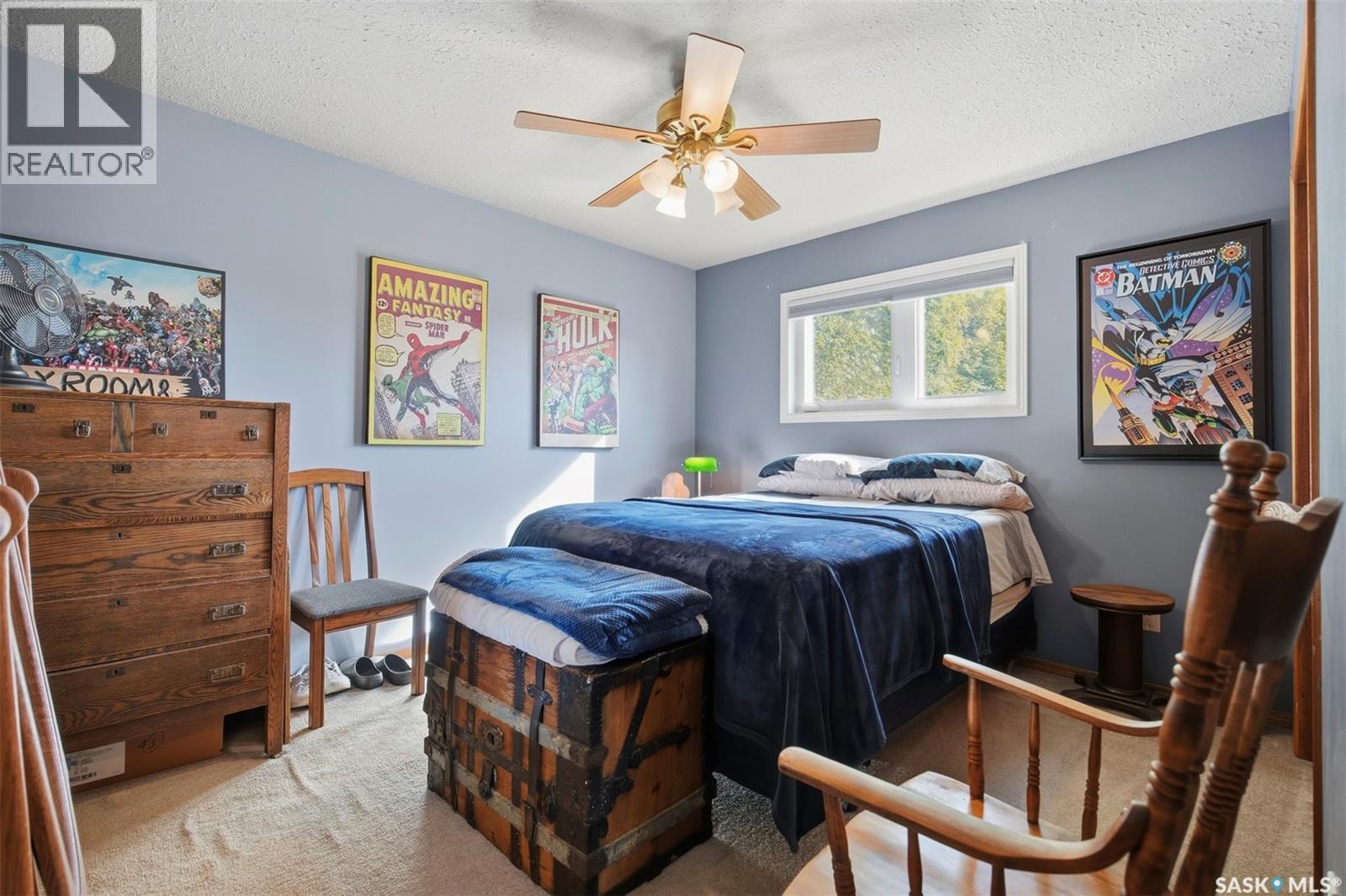 Bedroom with blue bedding, vintage wooden trunks, comic-book posters, and a ceiling fan.
