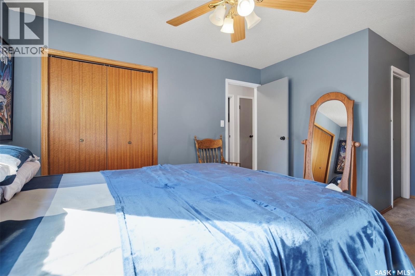 Furnished bedroom with a blue bedspread, wooden sliding closet doors, and a matching standing mirror.
