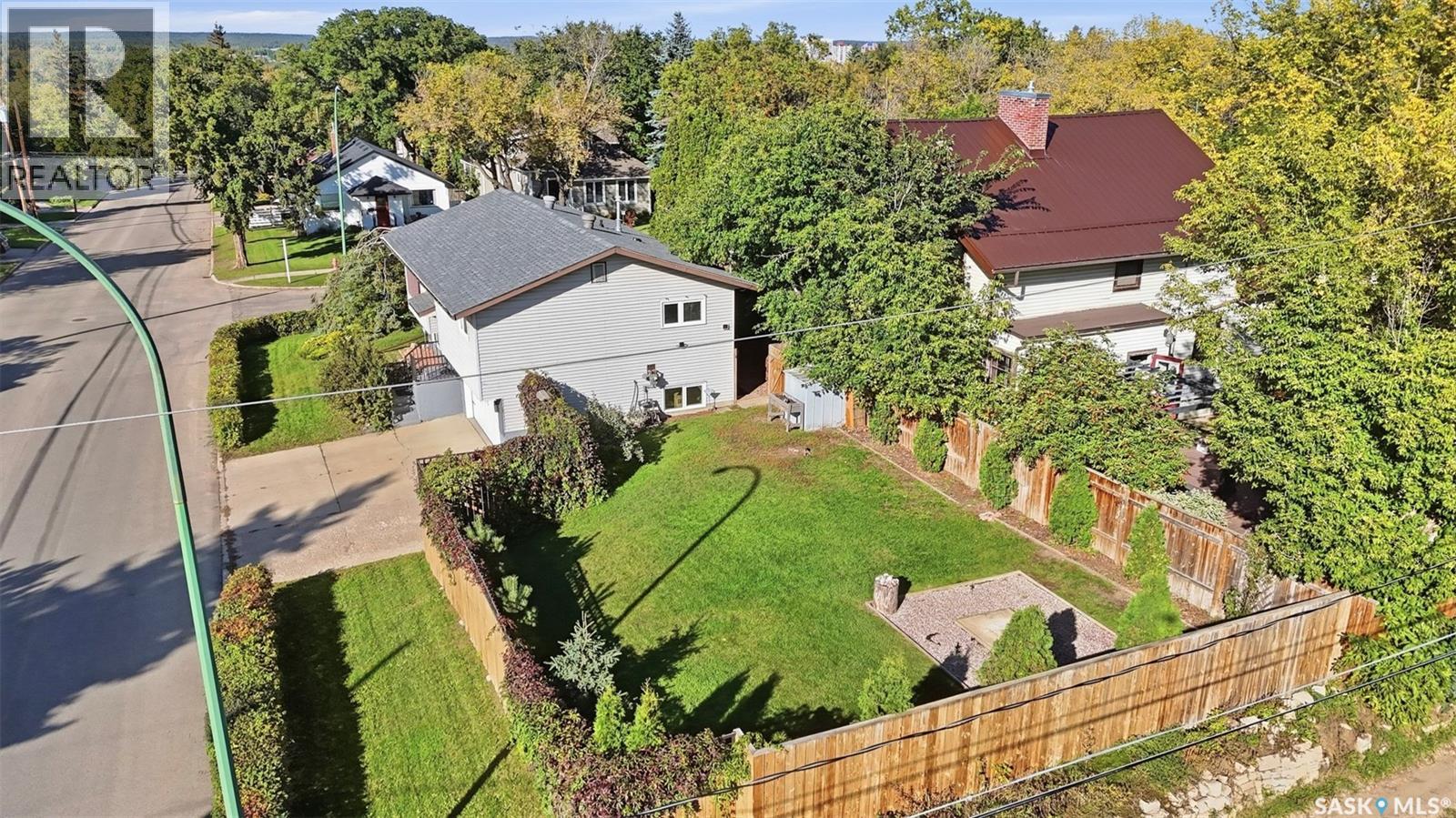 Aerial view of a fenced backyard with a broad lawn, patio, and neighboring homes.