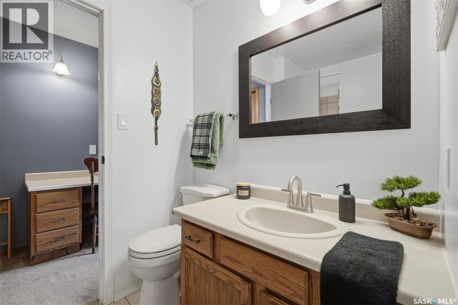 Bathroom with a wood vanity, oval sink, large mirror, and toilet beside an open doorway.
