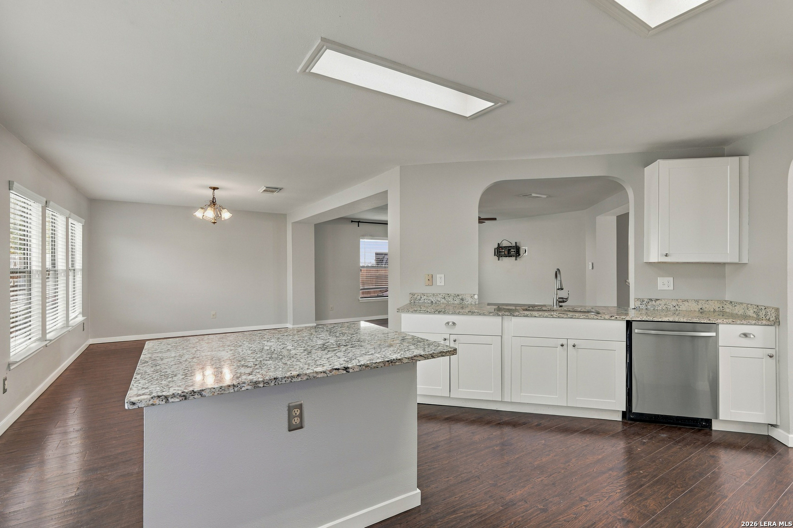 Open-plan kitchen with white cabinets, granite countertops, a large island, and dark wood floors.