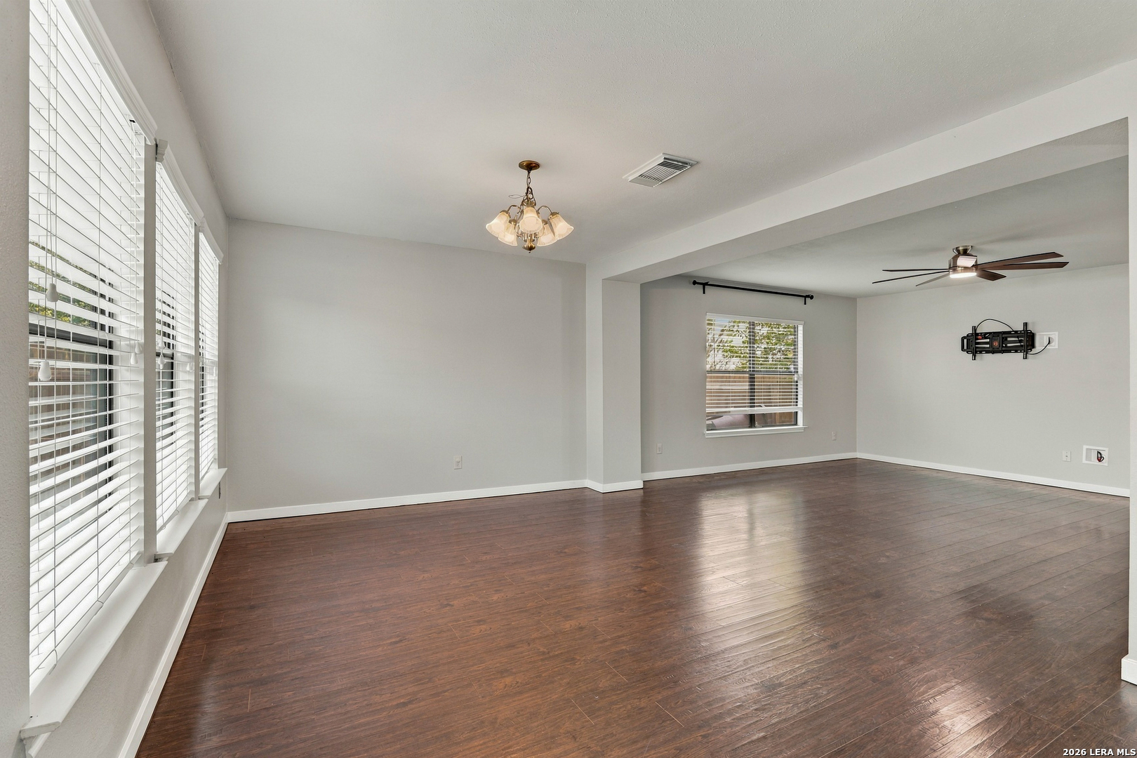 Empty living room with dark wood floors, large windows, and an open adjoining area.
