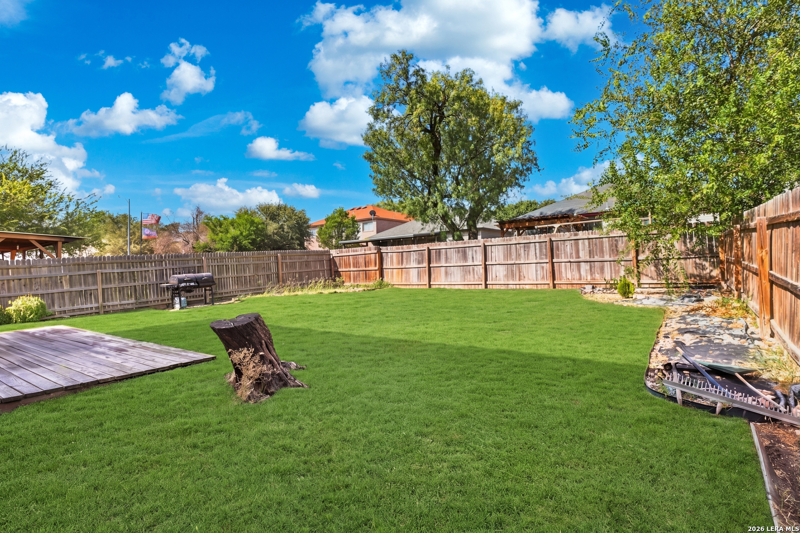 Fenced backyard with a broad lawn, wooden deck, and barbecue grill.