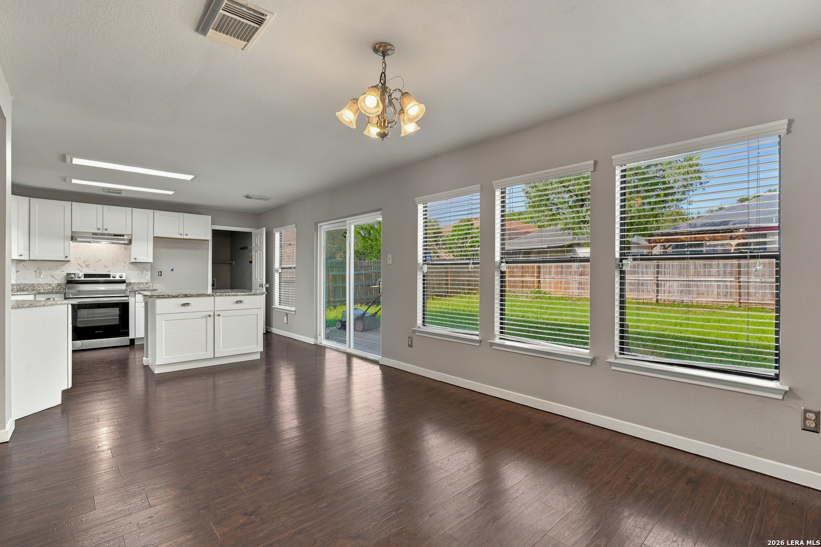 Open kitchen and dining area with white cabinets, dark flooring, and windows overlooking the backyard.