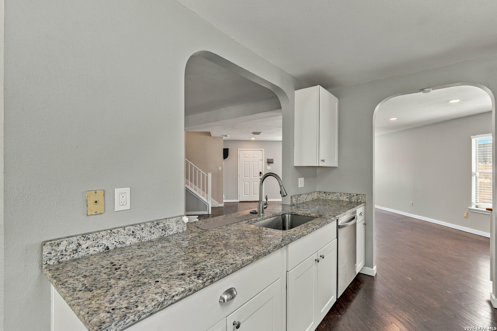 Kitchen with granite counters, white cabinets, a stainless sink, and arched openings to adjoining rooms.