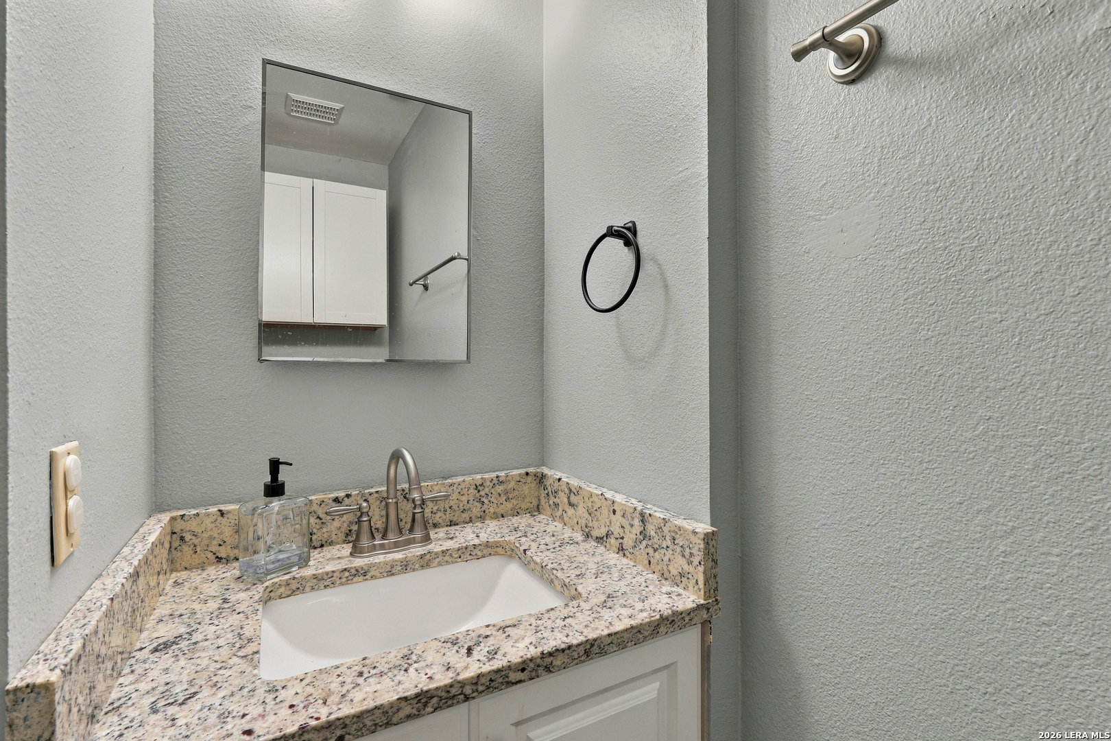 Bathroom vanity with a speckled granite countertop, white sink, metal faucet, and wall mirror.
