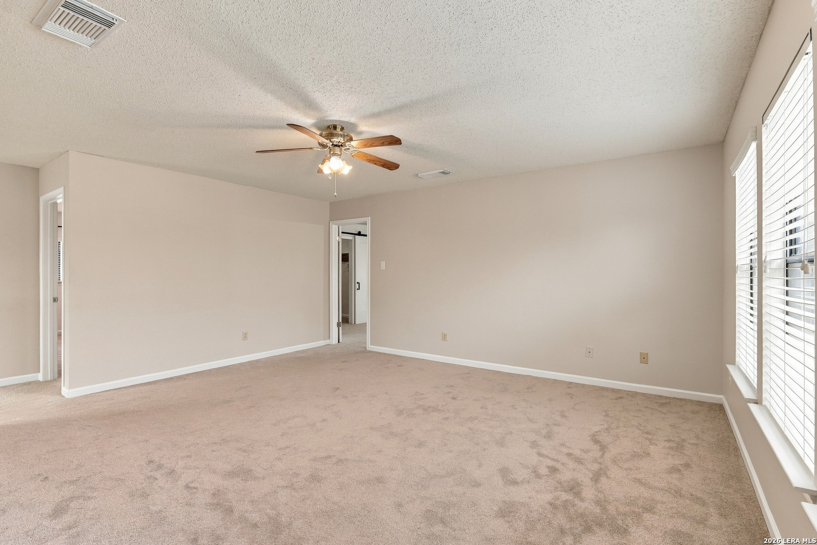 Vacant carpeted bedroom with a ceiling fan and tall windows with blinds.