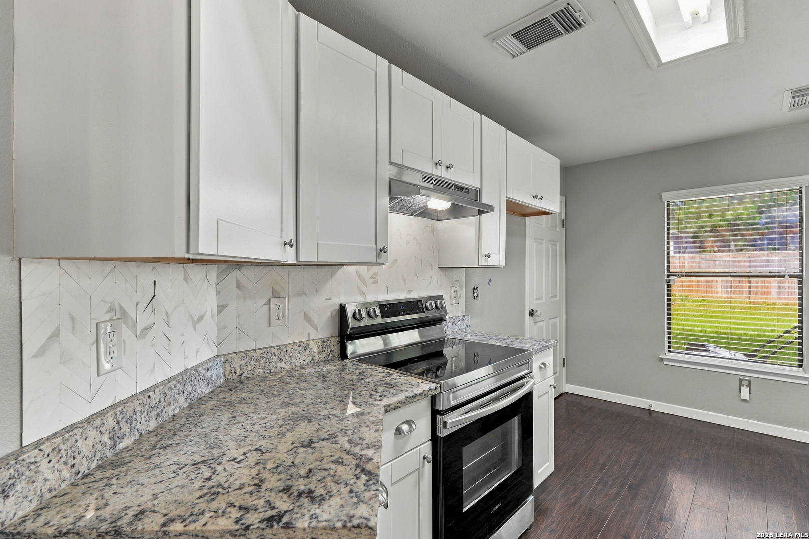 Kitchen with white cabinetry, a stainless steel range, patterned backsplash, and speckled countertops.