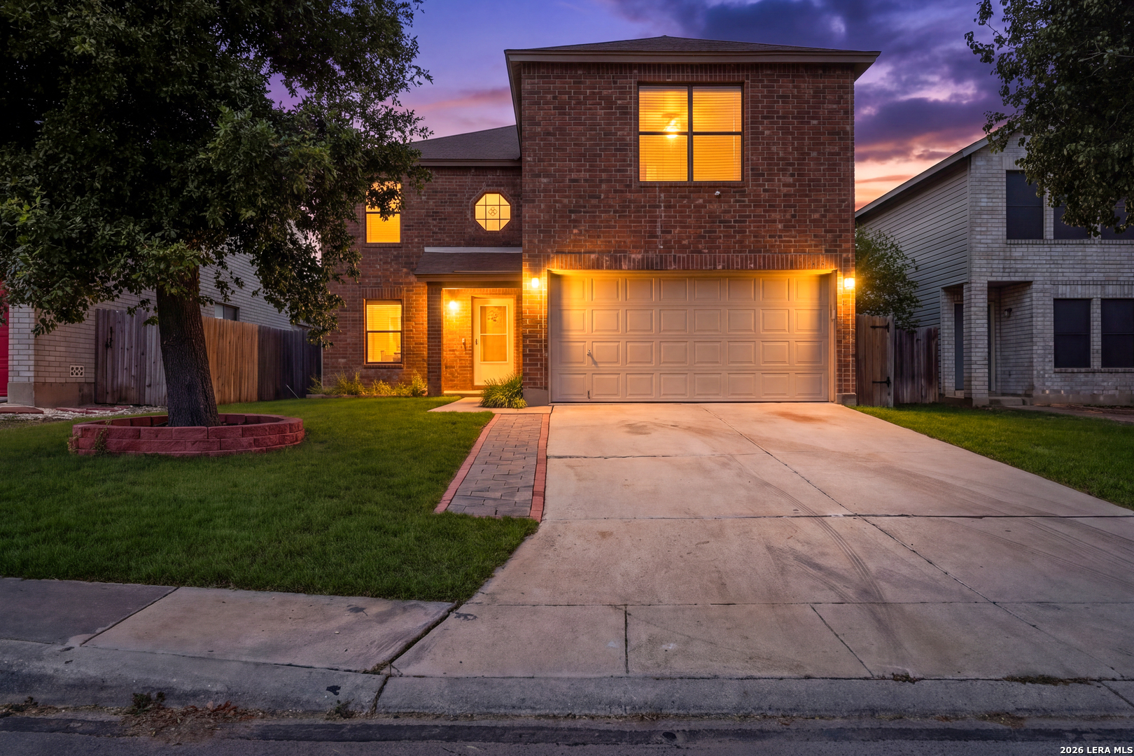 Two-story brick house with a lit entry, attached two-car garage, and wide driveway at dusk.