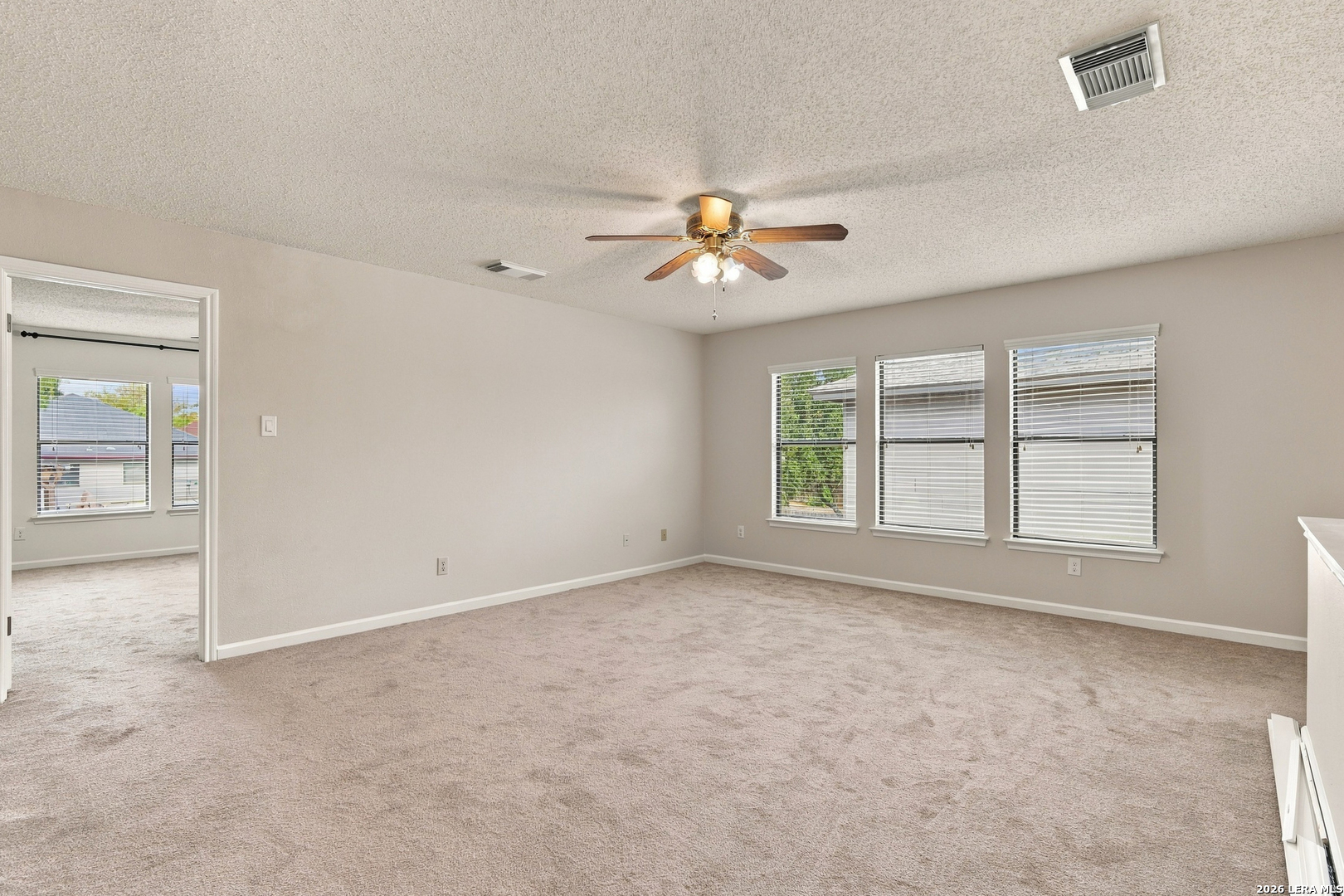 Empty carpeted room with a ceiling fan and three windows with blinds.