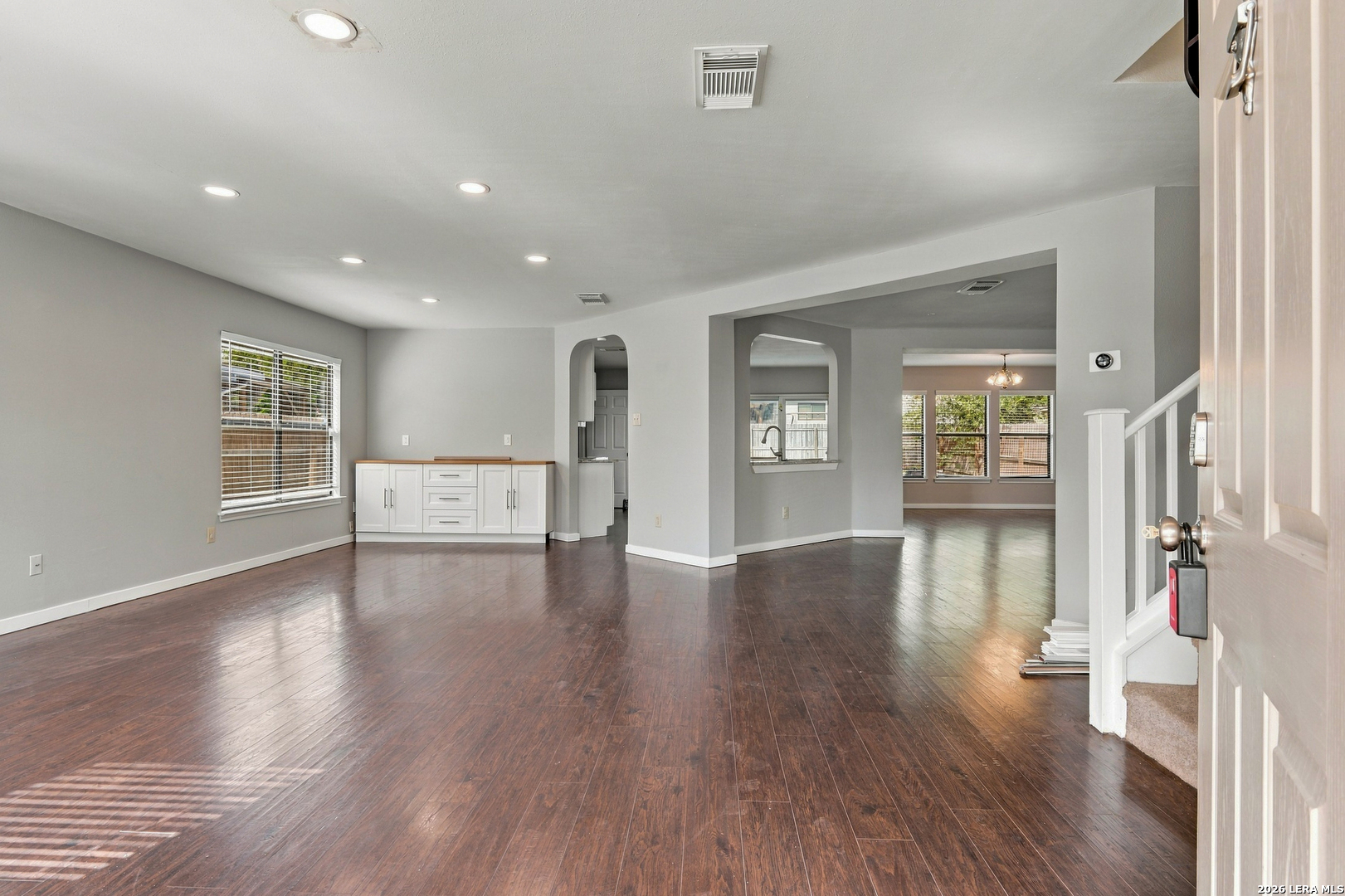 Empty living room with dark wood-look floors, a white built-in cabinet, and an open view to the dining area.