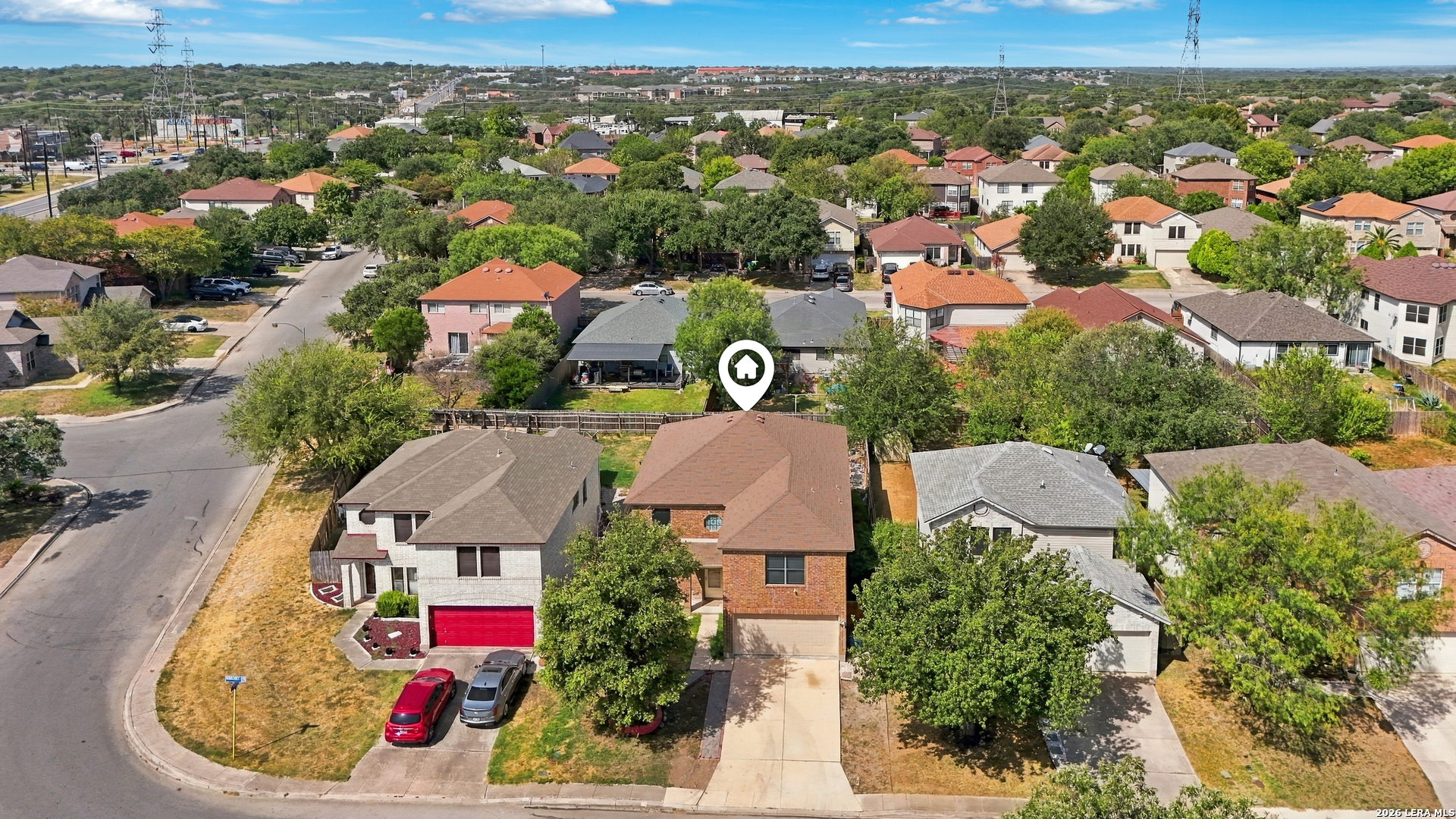 Aerial view of a two-story brick home with a tan roof, marked among neighboring houses.