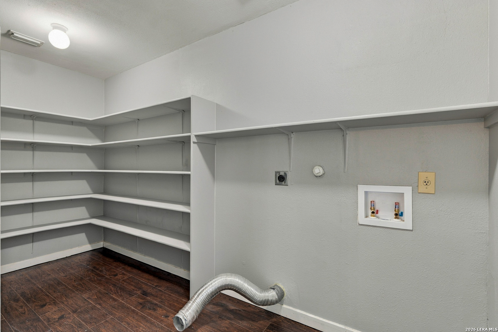 Empty laundry room with wraparound shelving, laundry hookups, and a flexible dryer vent hose.
