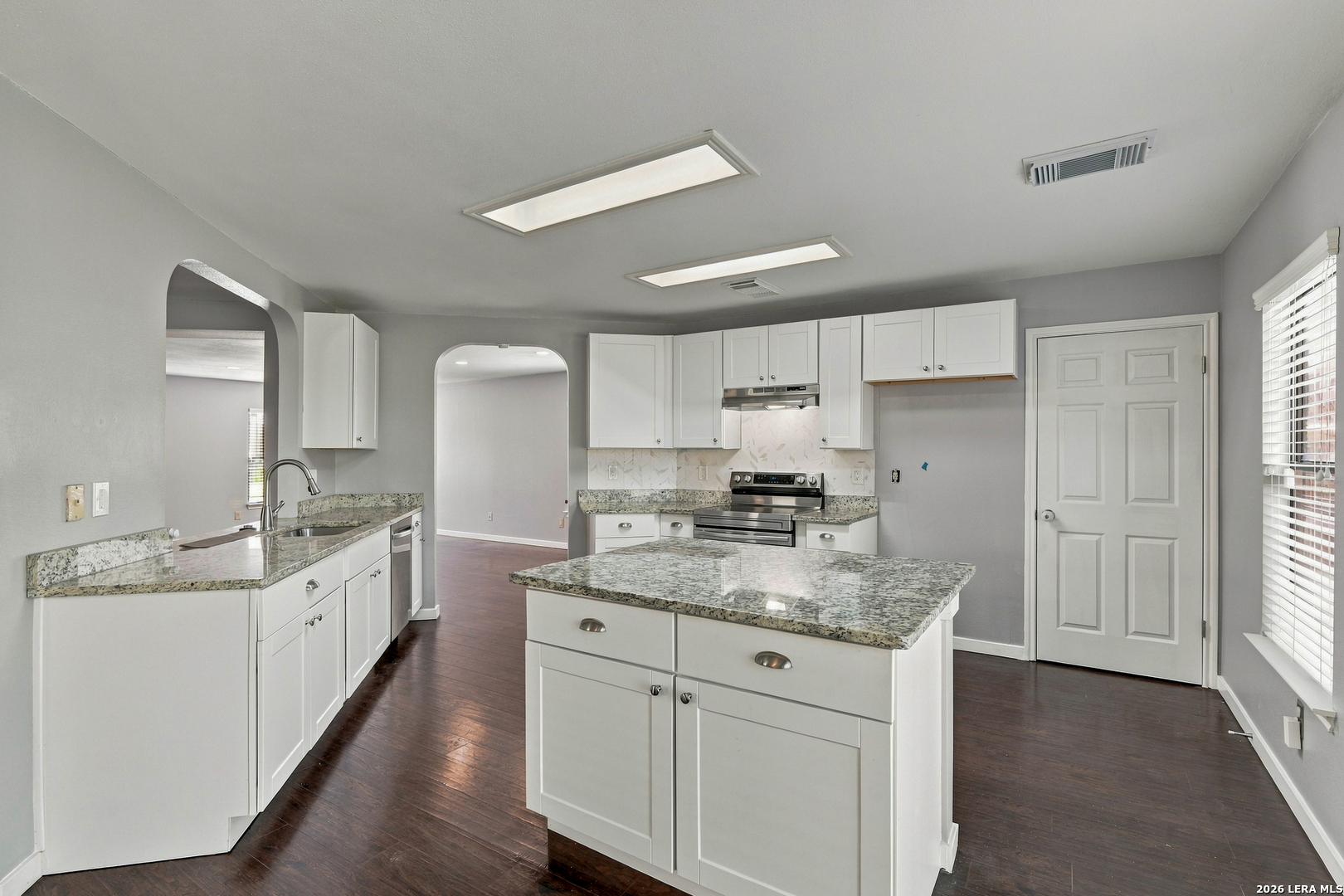 Kitchen with white cabinetry, granite counters, a large island, and stainless steel appliances.