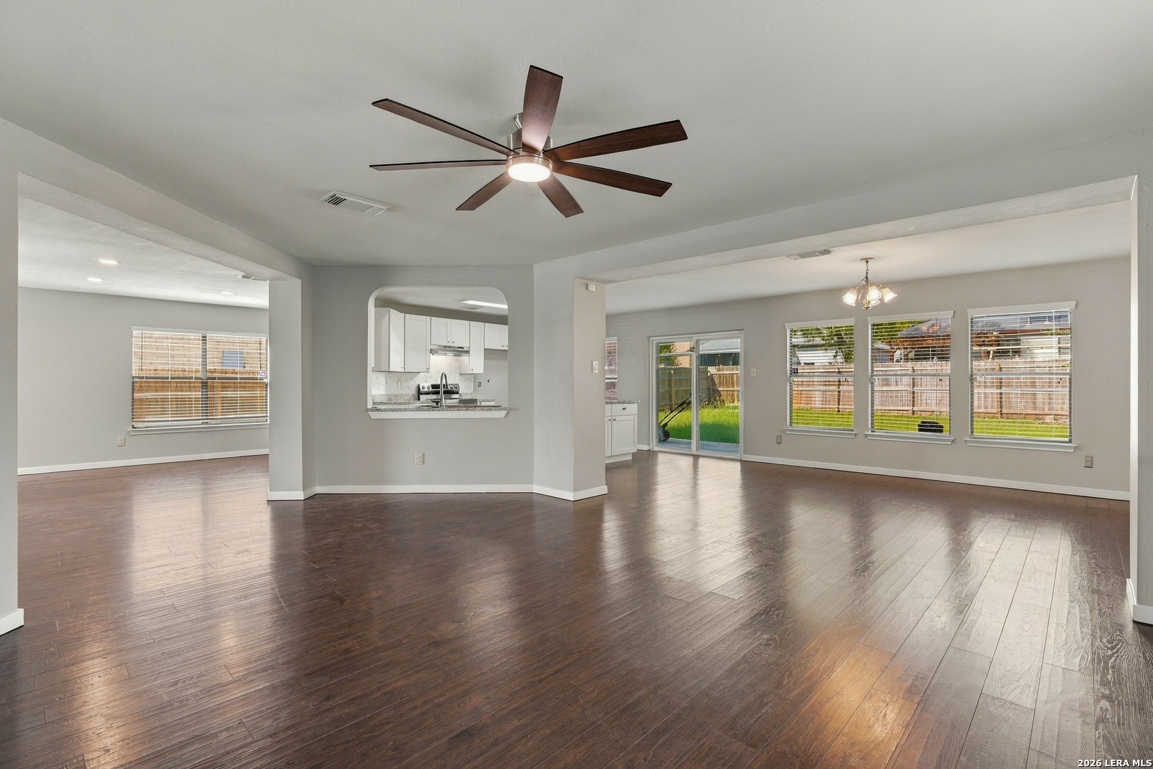 Open-plan living and dining area with dark wood floors, a pass-through kitchen, and sliding doors to the backyard.