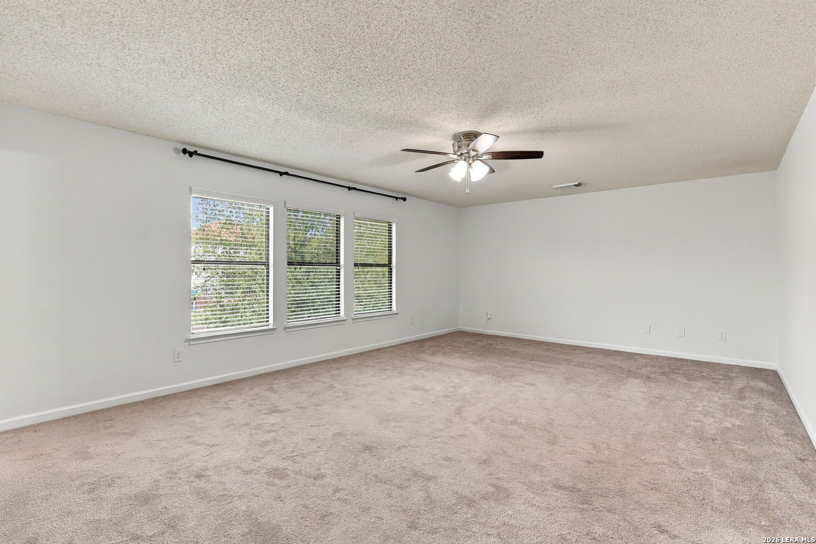 Vacant carpeted room with three windows and a ceiling fan.