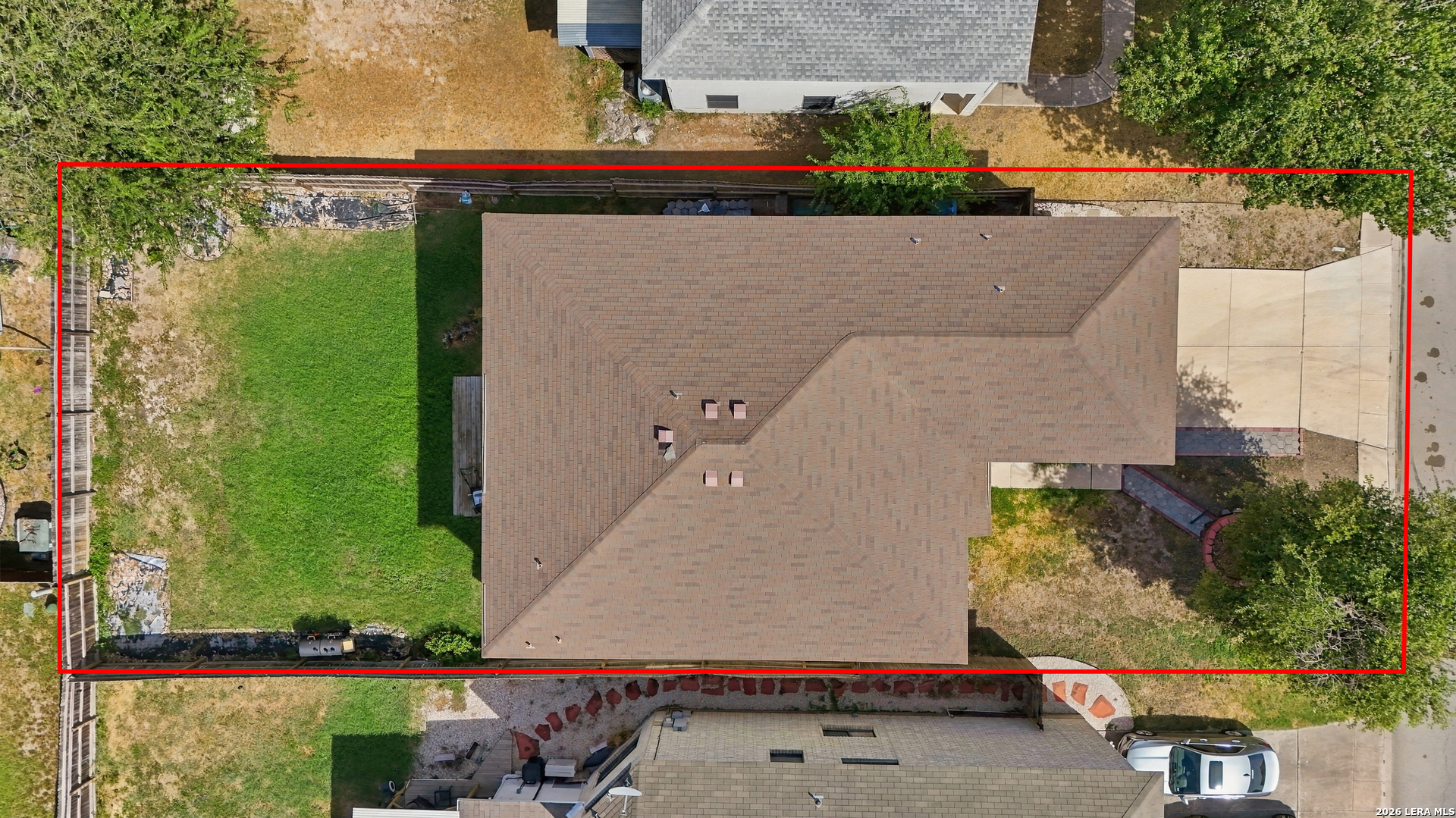 Aerial view of a home with a large shingle roof, green backyard, and concrete driveway, outlined in red.