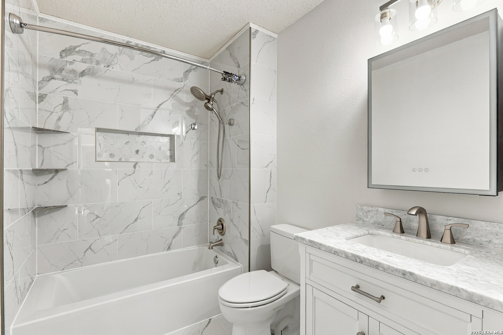 Bathroom with marble-look shower tile, bathtub, and white vanity with a stone-look countertop.