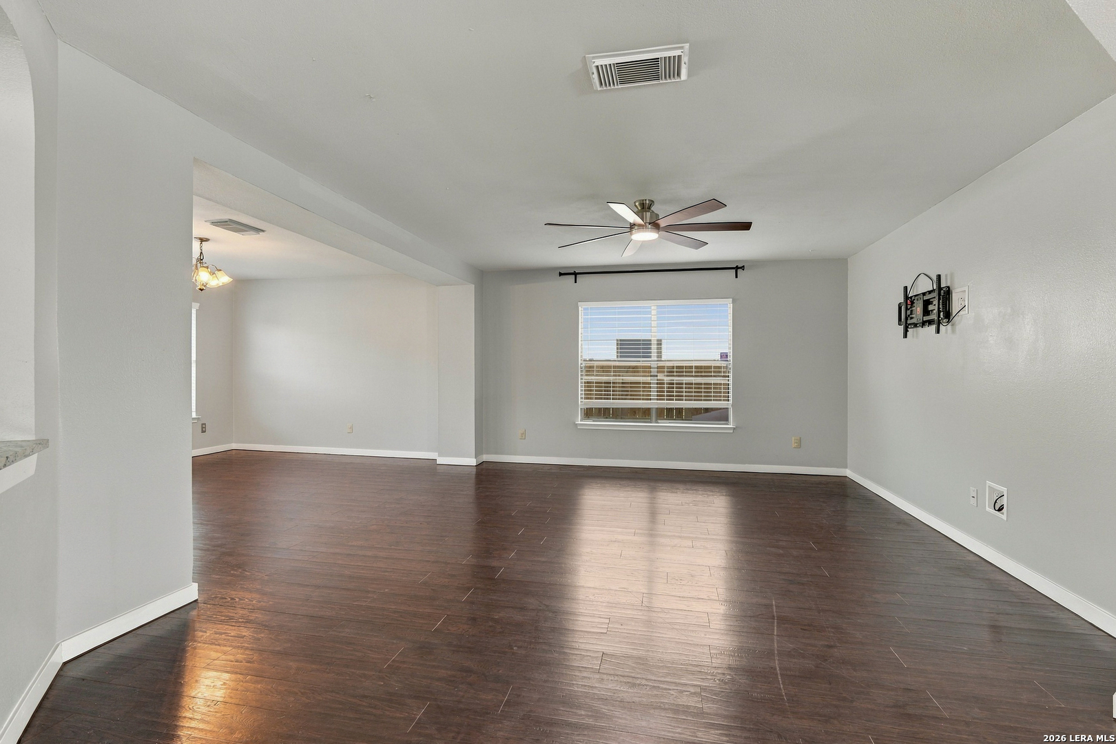 Vacant living room with dark wood floors, ceiling fan, and adjoining dining area.