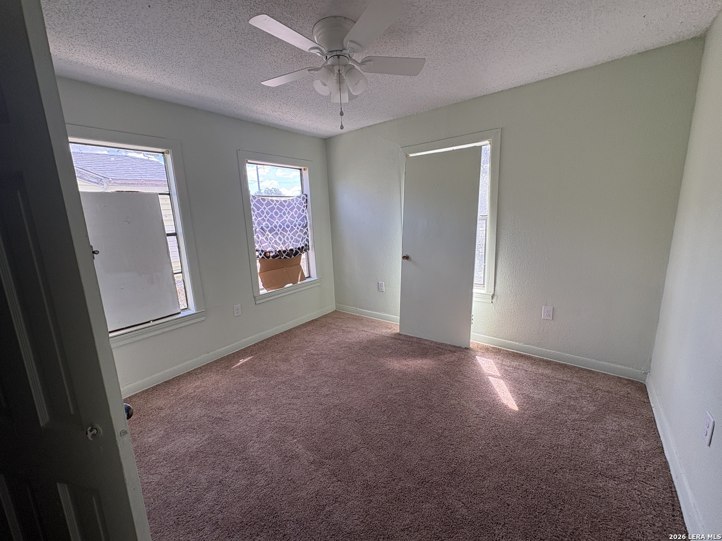 Empty carpeted bedroom with a ceiling fan and sunlight across the floor.