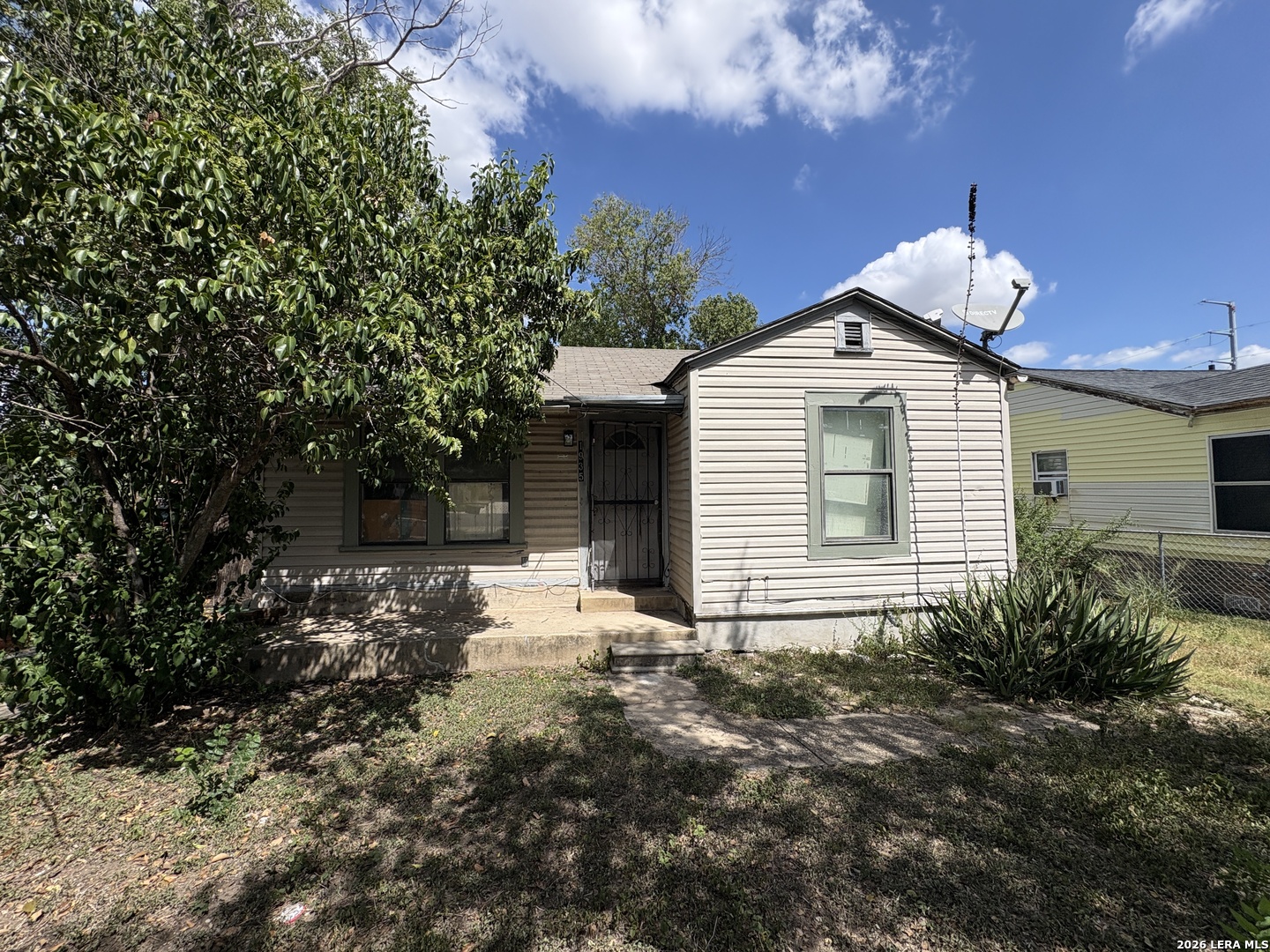 Single-story house with light siding, shaded front yard, and satellite dish.
