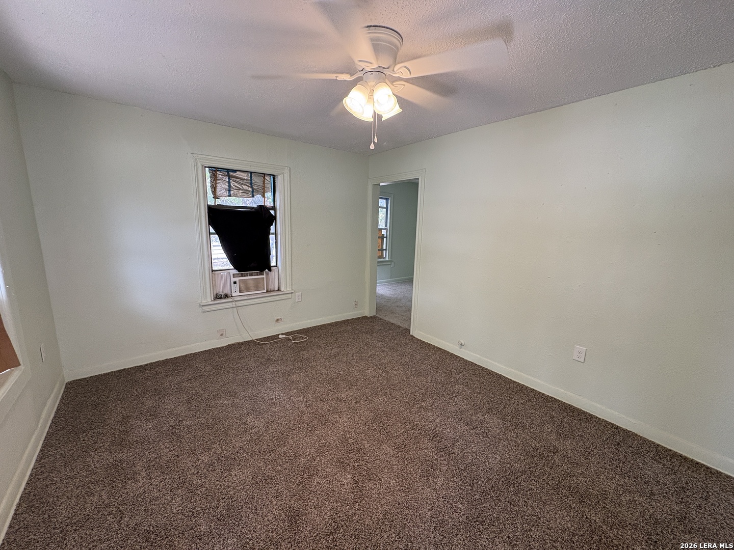 Empty carpeted bedroom with a ceiling fan, window air conditioner, and doorway to an adjoining room.