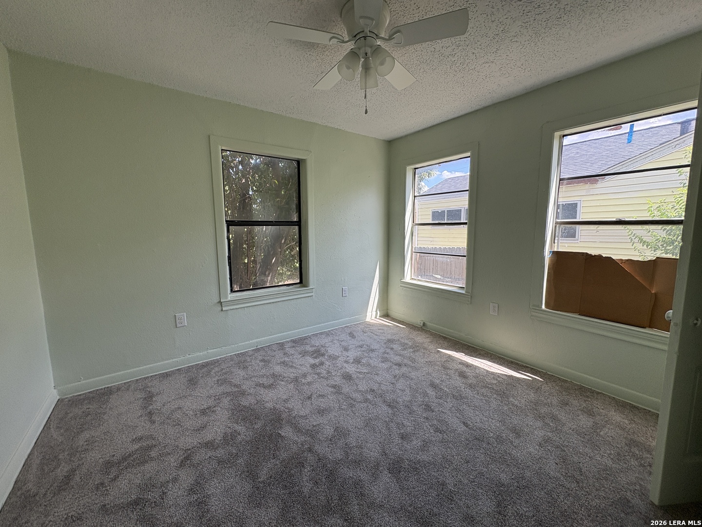 Empty bedroom with gray carpet, three windows, and a ceiling fan.