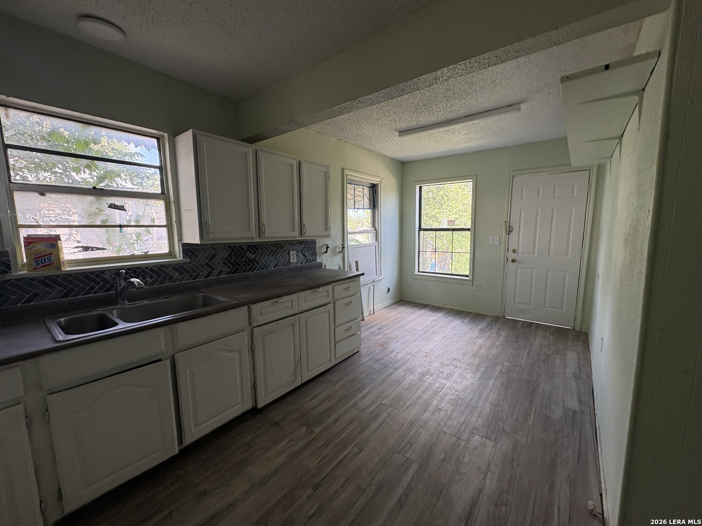 Unfurnished kitchen with pale cabinets, a dark herringbone backsplash, and wood-look floors.