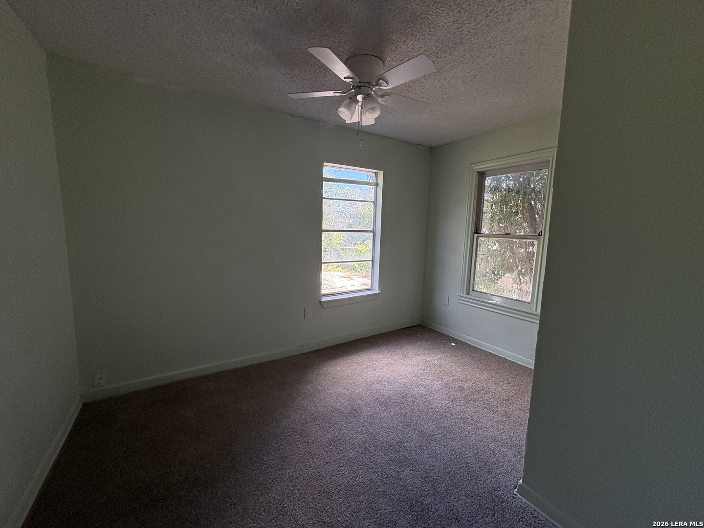 Empty carpeted bedroom with a ceiling fan and two windows.