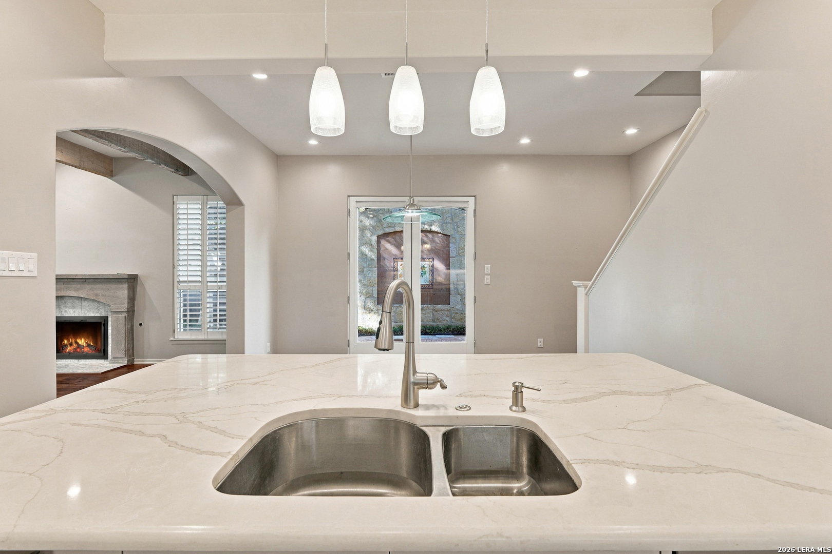 Kitchen with a large veined stone island, double sink, pendant lights, and an arched opening to a fireplace.